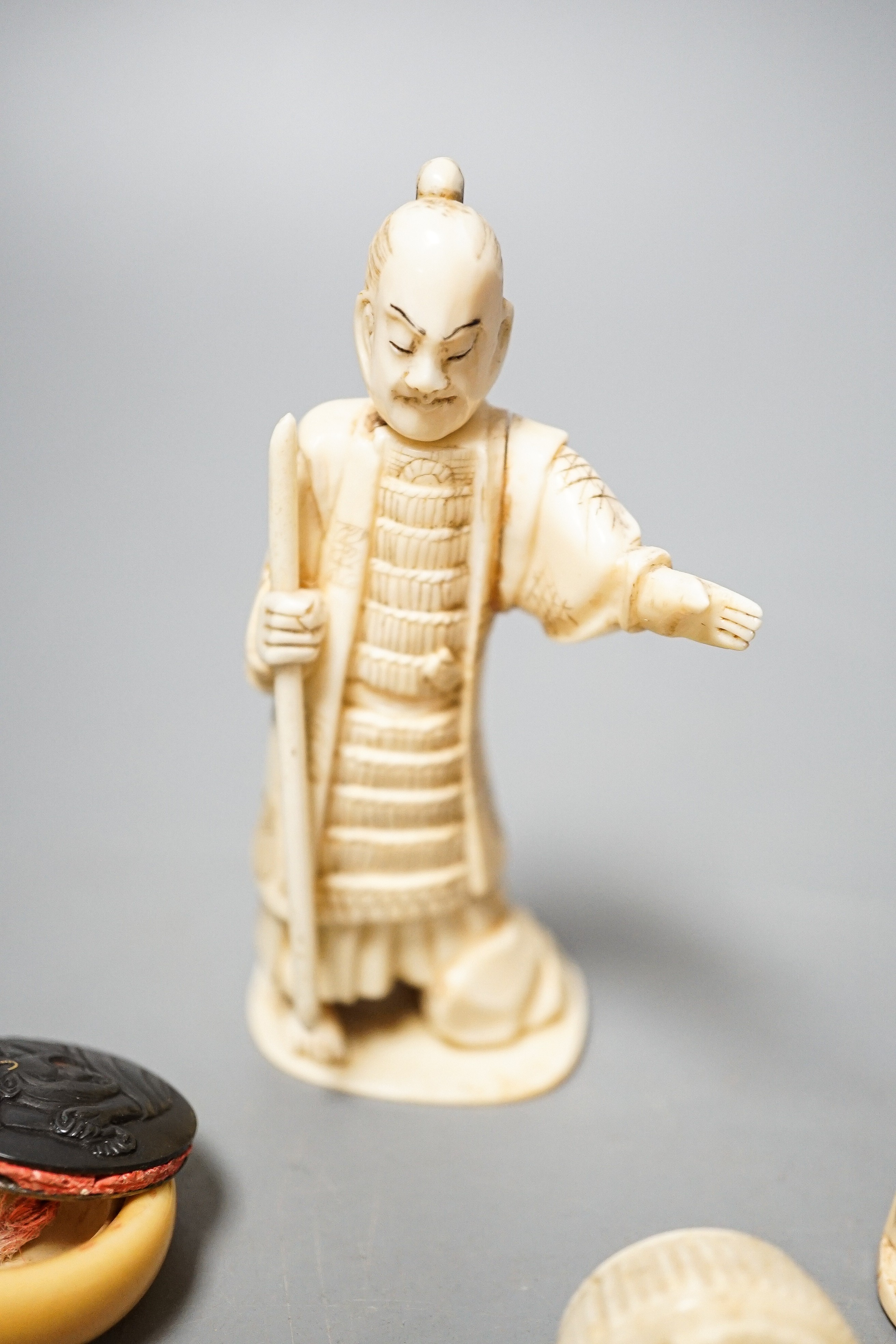 Three Japanese Ivory figures of men, a similar bezique marker, a Japanese staghorn single section inro with ivory manju, a Chinese ivory carving and a bone needlework container